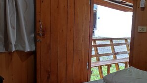 A wooden cabin room with a bed, a wooden door, and a view of a wooden deck outside. - chargevillage (Jiaoxi)