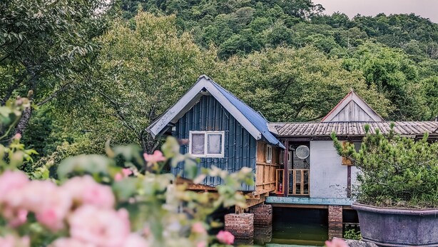A rustic wooden house with a balcony, surrounded by lush greenery and a pond. - chargevillage (Jiaoxi)