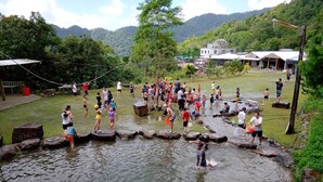 A group of people playing in a natural water setting with rocks and a grassy area, surrounded by trees and a mountainous backdrop. - chargevillage (Jiaoxi)