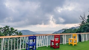 A balcony with a wooden railing and three chairs in blue, red, and yellow. - chargevillage (Jiaoxi)