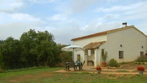 Un edificio blanco con techo de tejas, un patio con mesa y sillas, y plantas en macetas.