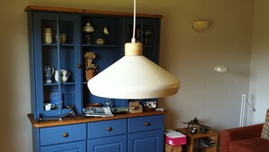 Una mesa de comedor de madera con sillas, un armario azul con utensilios de cocina, una lámpara colgante y un sofá rojo.