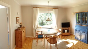 Una habitación acogedora con una mesa de comedor de madera, sillas, un mueble con televisor y una ventana con cortinas.