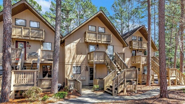 A cabin-style lodging with a central staircase, wooden balconies, and a forested backdrop.