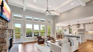 A spacious living area with a fireplace, large windows, and a modern kitchen. - Coveside Spacious 5BR Waterfront Home (Six Mile)