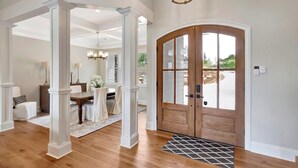 A spacious foyer with a wooden door, white columns, and a dining area with a table and chairs. - Coveside Spacious 5BR Waterfront Home (Six Mile)