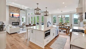 A spacious kitchen with a large island, white cabinetry, and a stone fireplace. - Coveside Spacious 5BR Waterfront Home (Six Mile)
