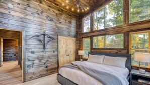 Un dormitorio con una cama grande, paredes de madera, una ventana y una mesita de noche.