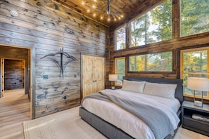 A bedroom with a large bed, wooden walls, a window, and a nightstand.