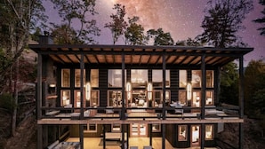 Una cabaña de madera de varios niveles con ventanas amplias, una terraza y vistas al cielo nocturno.