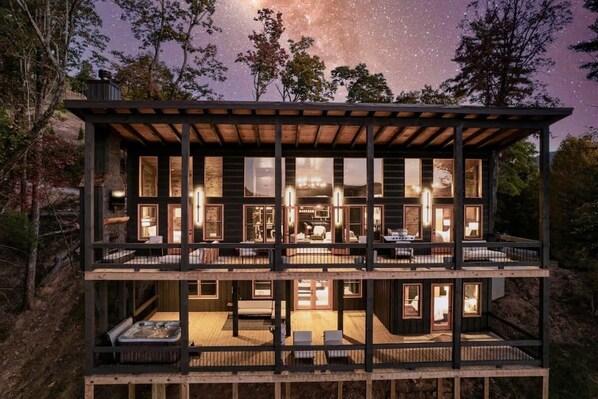 Una cabaña de madera de varios niveles con ventanas amplias, una terraza y vistas al cielo nocturno.