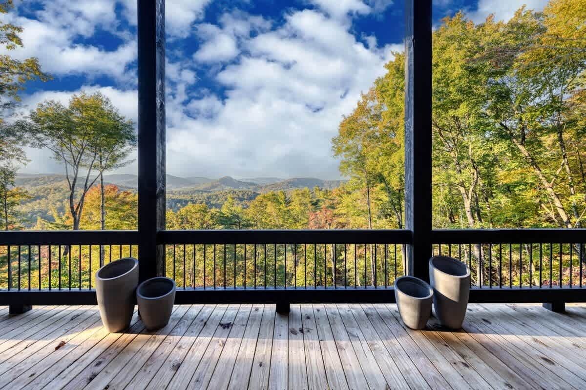A wooden deck with a railing, two planters, and a view of trees and mountains.