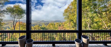 A wooden deck with a railing, two planters, and a view of trees and mountains.