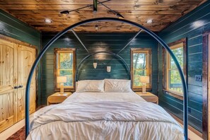 Un dormitorio con techo abovedado, paredes de madera, una cama, dos mesitas de noche con lámparas y ventanas.