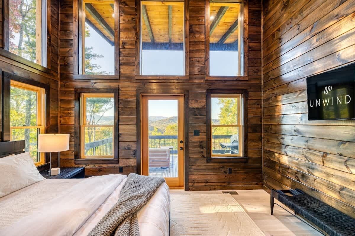 Une chambre située dans une cabane en rondins, avec un lit, une télévision et plusieurs fenêtres.