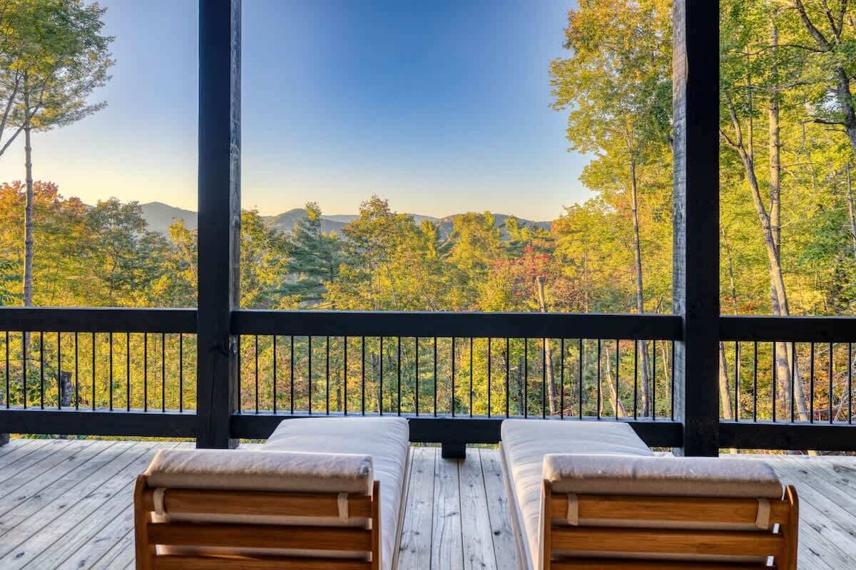 A wooden deck with two wooden chairs and a view of a forested mountain range.
