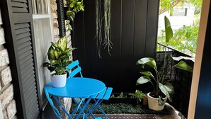 Une petite terrasse avec une table et des chaises bleues, des plantes en pot, une plante suspendue et un tapis à rayures tigrées.