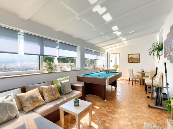 A spacious living area with a pool table, comfortable seating, and large windows offering a view of the city.