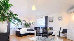 Ein modernes Wohnzimmer mit einem weißen Sofa, schwarzen Sesseln, einem Esstisch und einer großen Pflanze.