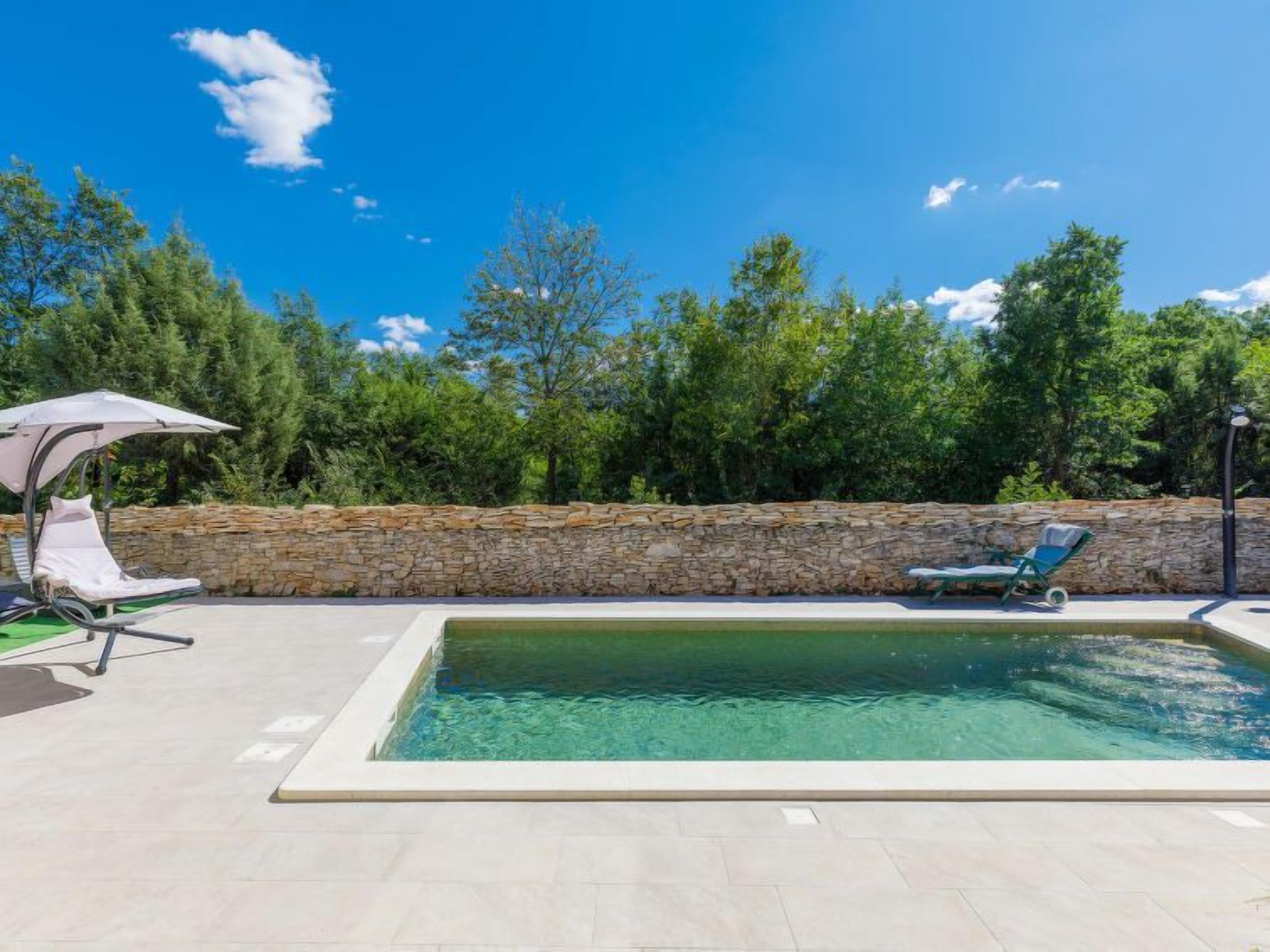 Ein Swimmingpool mit zwei Liegestühlen und einer Steinmauer im Hintergrund.
