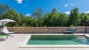 Ein Swimmingpool mit zwei Liegestühlen und einer Steinmauer im Hintergrund.