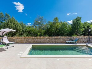 A swimming pool with two lounge chairs and a stone wall in the background. - Vacation home Marija by Interhome (Pula/Vodnjan)