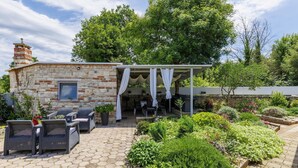Ein Steinhaus mit überdachter Terrasse, Sitzgelegenheiten im Freien und einem Garten.