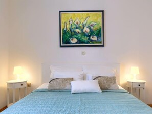 A bedroom with a bed, white bedding, two bedside tables with lamps, and a painting on the wall.
