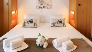 A hotel room with a large bed, two pillows with a mountain and ski lift design, a painting of a deer, and two rolled towels on the bed. - Muverans I C3 by Interhome (Nendaz)