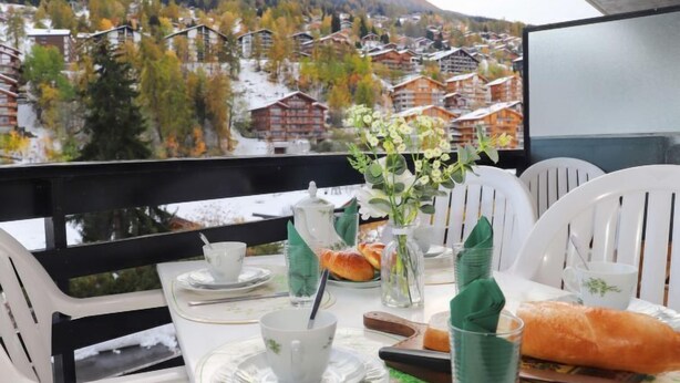 A dining table set with a cup, saucer, napkin, glass, and a baguette, overlooking a mountainous village. - Muverans I C3 by Interhome (Nendaz)