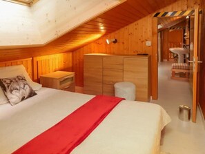 A cozy bedroom with a wooden ceiling, a bed with a red blanket, a nightstand, and a wardrobe.