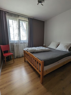Une chambre à coucher avec un lit en bois, une chaise rouge et une fenêtre avec des rideaux.
