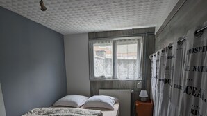 Et soveværelse med en seng, et vindue, et natbord og et gardin.