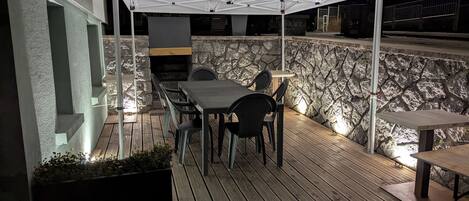 An outdoor patio with a stone wall, a table and chairs, and a grill area.