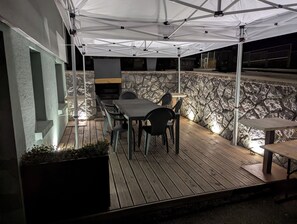 Um pátio externo com parede de pedra, uma mesa e cadeiras, e área de churrasco.