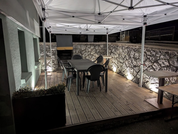 An outdoor patio with a stone wall, a table and chairs, and a grill area.