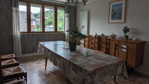 En spisestue med et stort bord, stole, en potteplante og et billede på væggen.