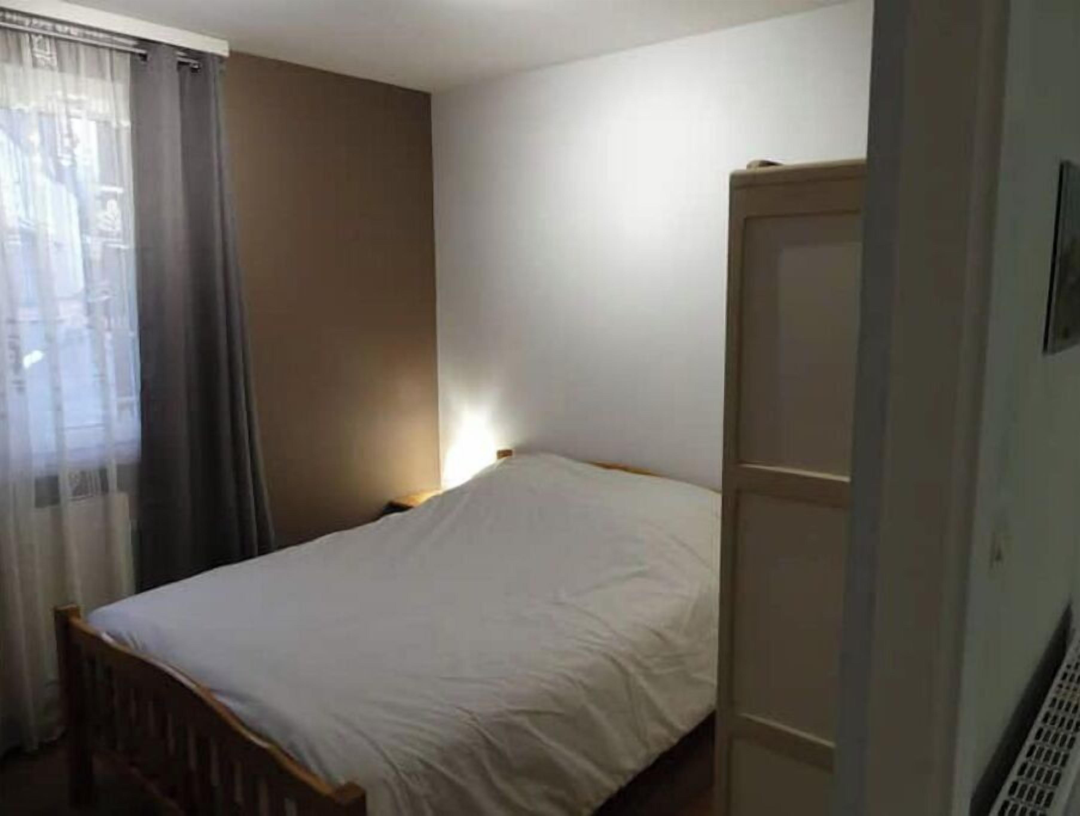 Una habitación pequeña con una cama individual, cabecera de madera, mesita de noche y ventana con cortinas.