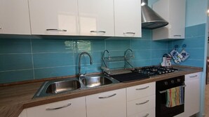 Una cocina con armarios blancos, un lavamanos de acero inoxidable, una estufa a gas y un horno negro.