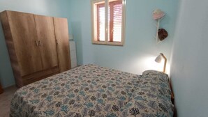 Un dormitorio con cama, armario, ventana con persianas y una lámpara fijada a la pared.