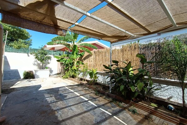 An outdoor patio area with a thatched roof, a stone pathway, and various plants.