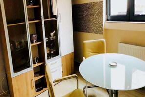A room with a glass-top table, a chair, a cabinet with shelves, and a radiator.