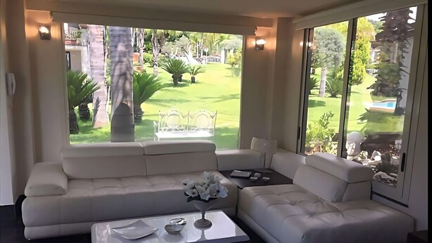 A modern living room with a sectional sofa, a coffee table, and a view of a well-maintained garden through large windows.