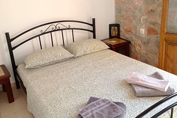 A bed with a patterned bedspread, a nightstand with a framed picture, and a stone wall. - Inviting apartment in Galaxidi with balcony (Galaxidi)