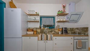 Eine kleine Küche mit weißen Schränken, einem Einbauofen, einem Spülbecken mit dekorativer Fliesenrückwand und einem Fenster mit Spitzenvorhang.