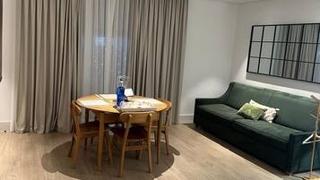 Een moderne woonkamer met een ronde houten tafel, een groene bank en een groot raam met gordijnen.