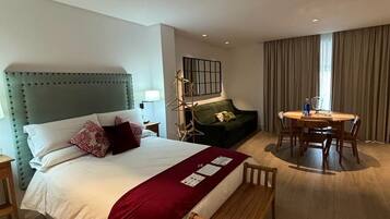 Una habitación de hotel con cama, sofá verde, mesa de comedor con sillas y un banco de madera.