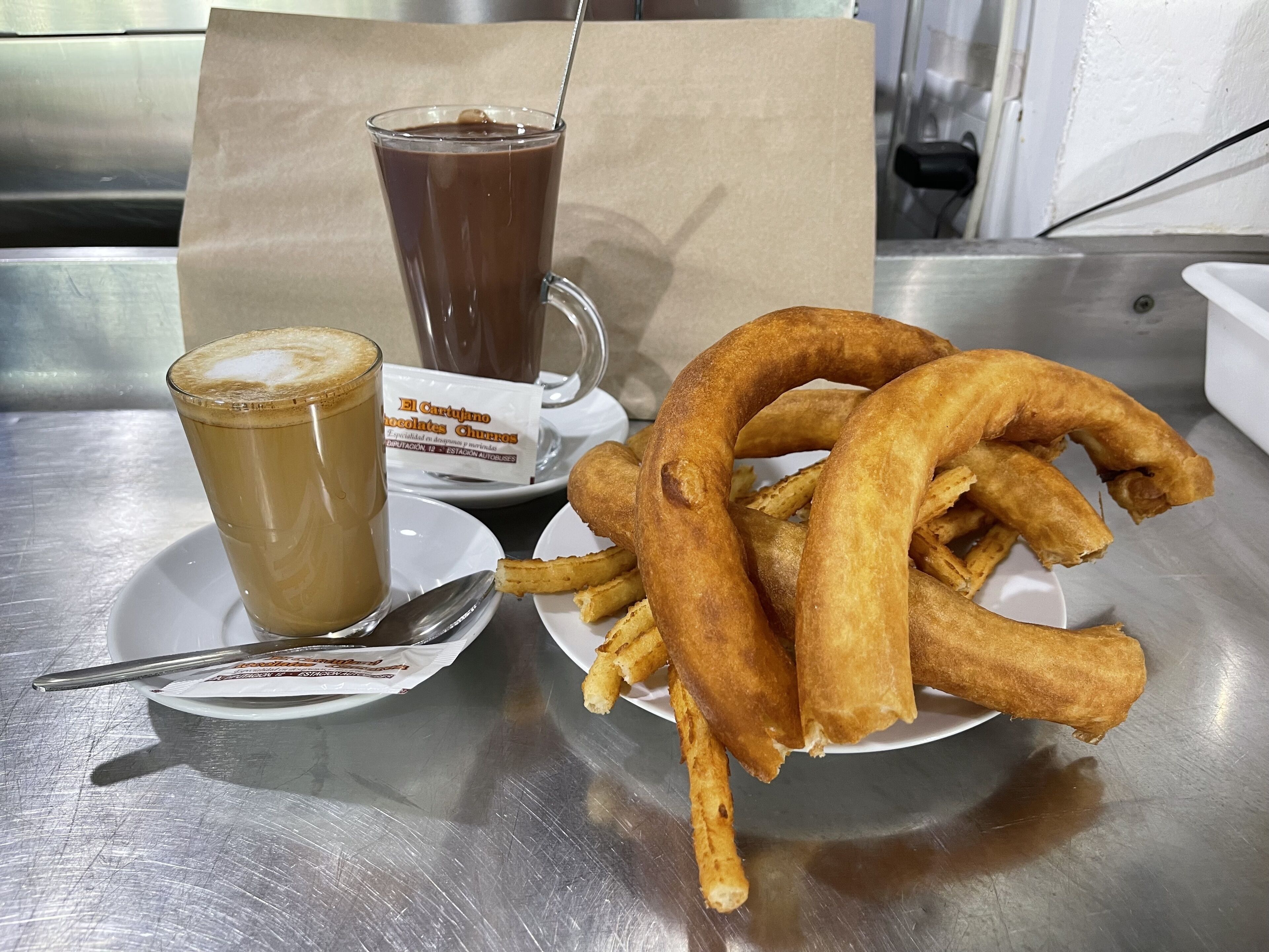 Un tavolo con un bicchiere di caffè ghiacciato, un bicchiere alto di cioccolata calda e un piatto di churros.