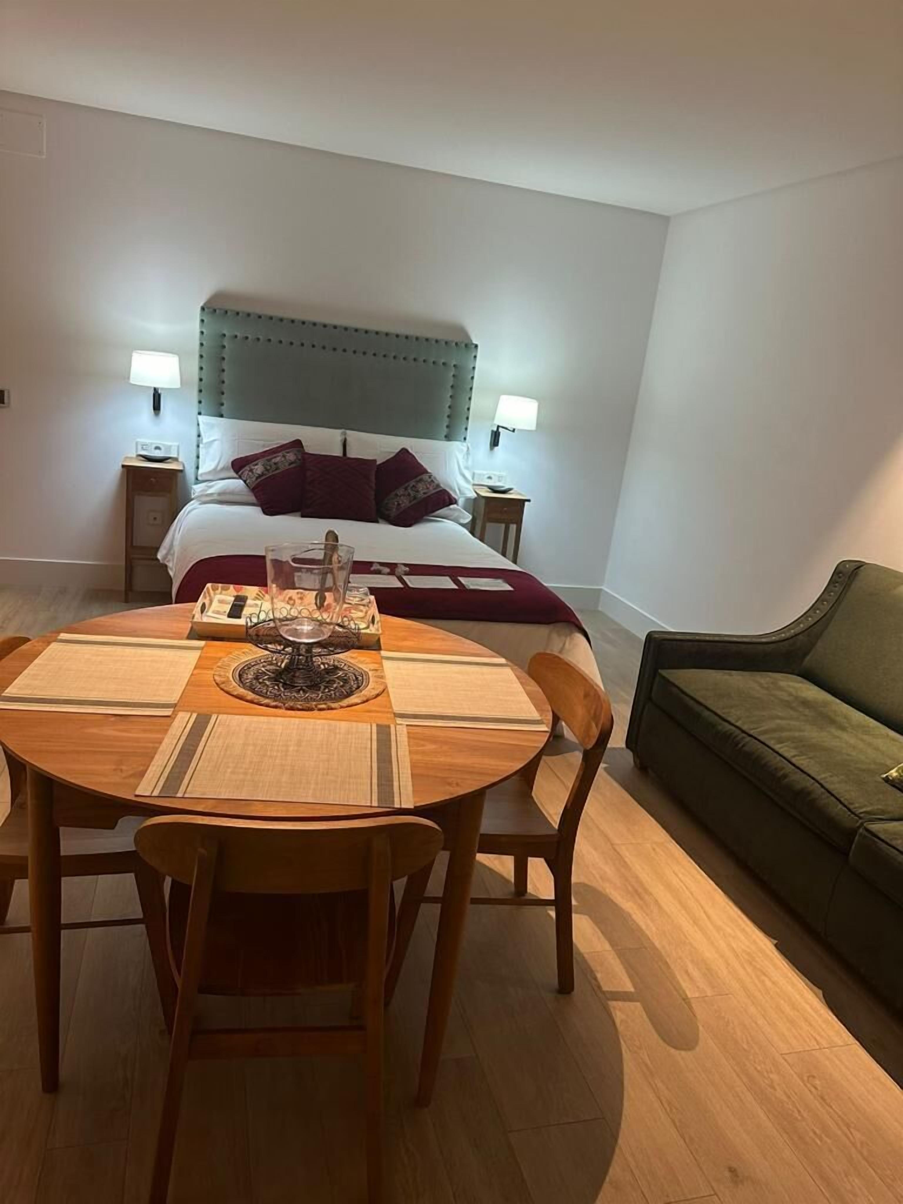 Una habitación de hotel con cama, mesitas de noche, una mesa de comedor con sillas y un sofá verde.