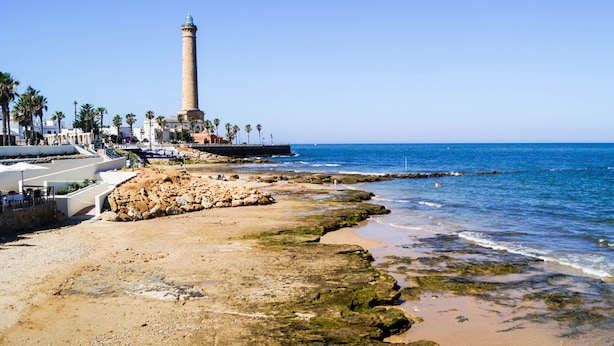 A coastal area with a lighthouse, rocky shoreline, and a paved walkway along the beach. - Apartamentos Turísticos La Plaza (Chipiona)